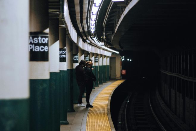 A lone person waits at Astor Place subway station platform in New York City, showcasing urban transit.